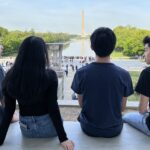 Thumbnail of http://Four%20students%20sit%20looking%20at%20Washington%20Monument.