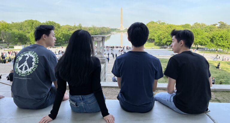 Four students sit looking at Washington Monument.