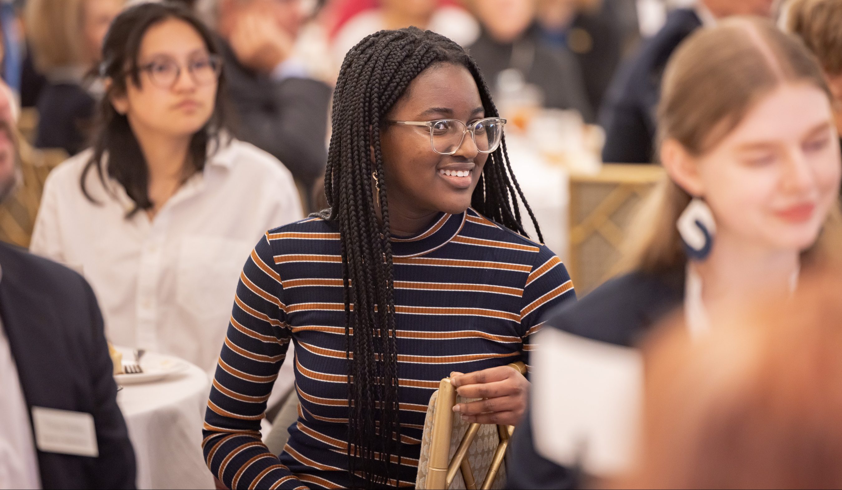 A student sits at a table surrounded by other students at a large event.